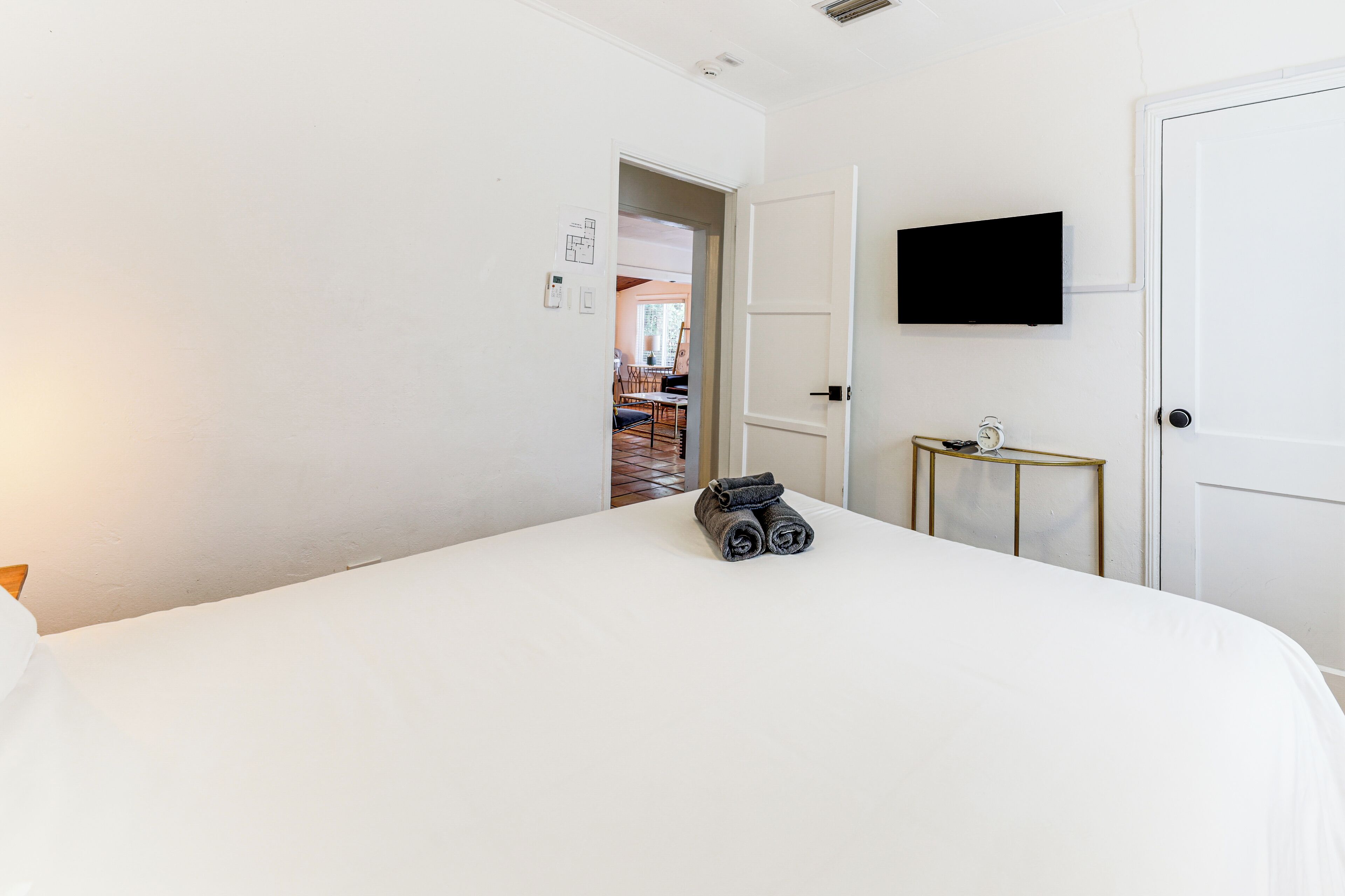 Ein Hotelzimmer mit einem großen Bett, einem an der Wand befestigten Fernseher und einer Tür zu einem weiteren Raum.