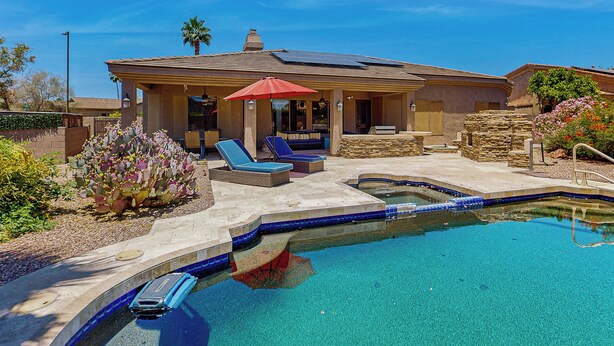 A pool area with lounge chairs, a covered patio, and a stone wall. - Goodyear Home w/ Private Pool, Spa & Built-in BBQ (Goodyear)