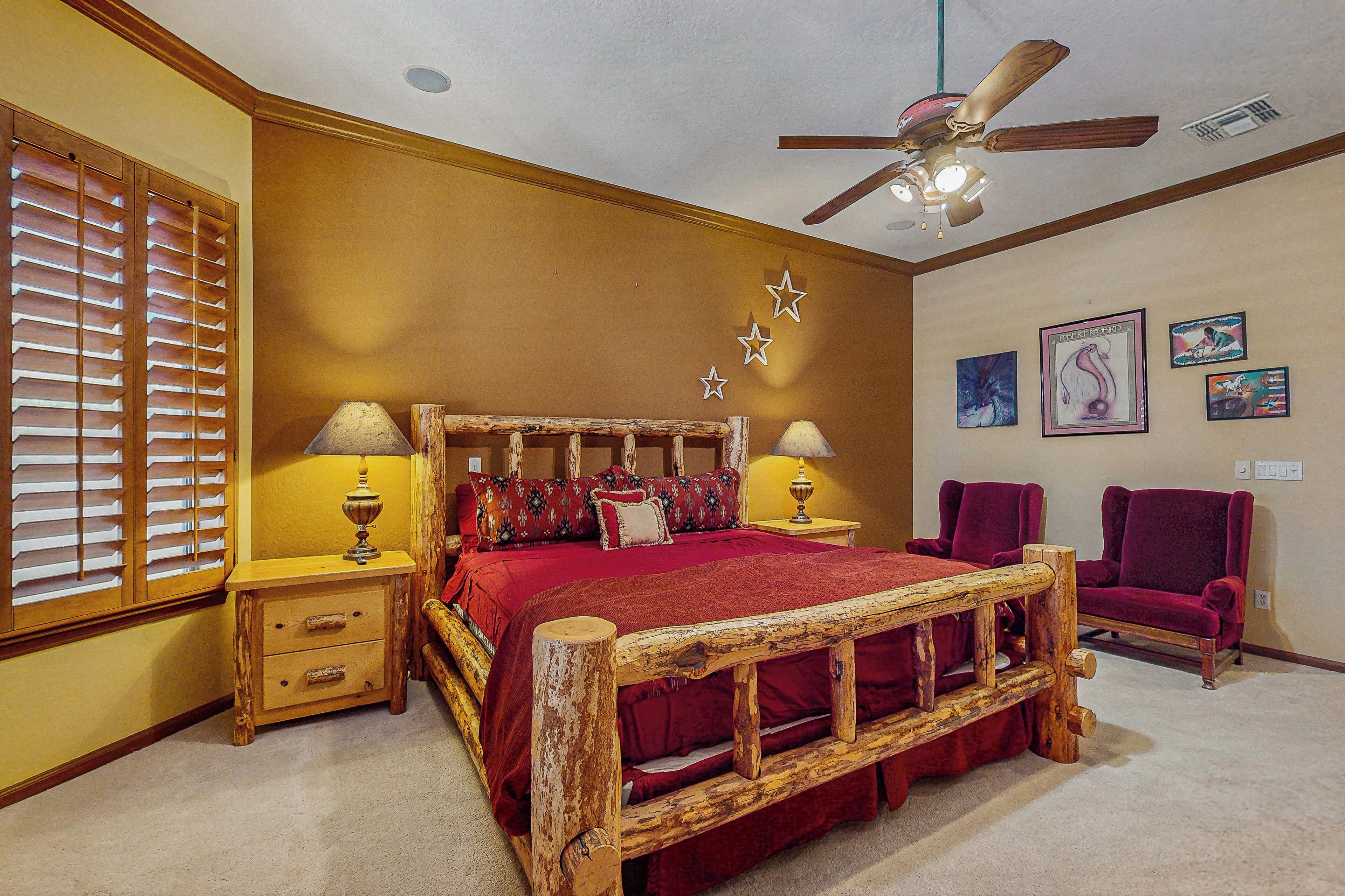 Quarto com estrutura de cama de madeira, duas mesas de cabeceira, ventoinha no teto e janela com persianas.