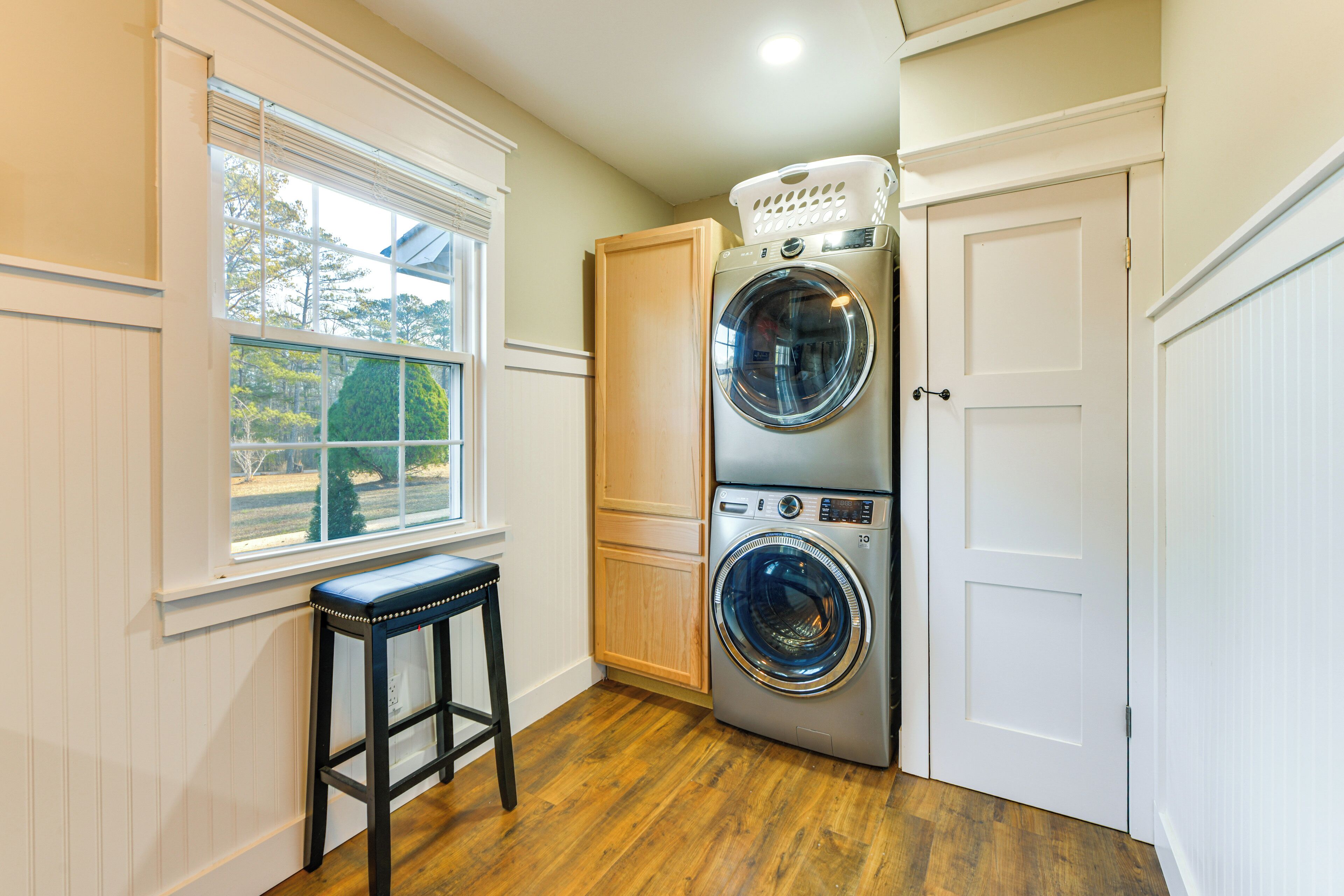 A laundry room with two stacked washers and dryers, a wooden bench, and a window with blinds.