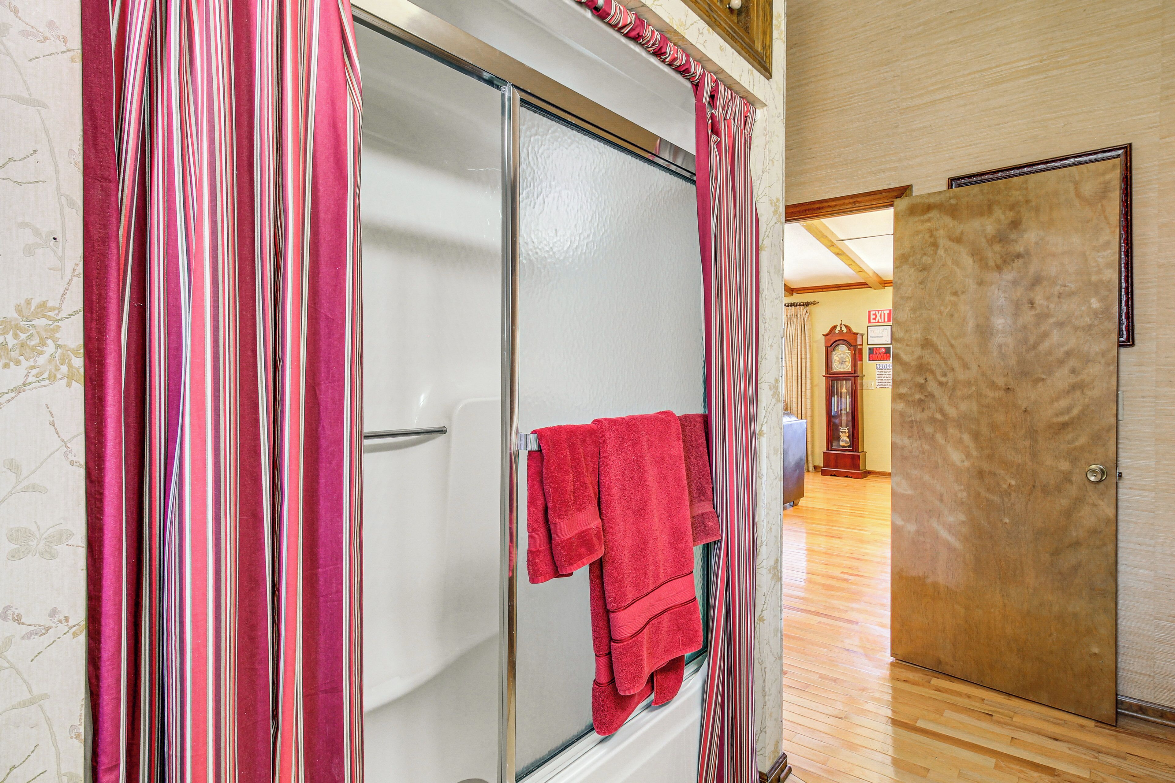 A bathroom with a glass shower door, a red towel hanging on the door, and a wooden floor.