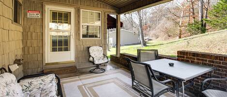 A covered porch with a dining table and chairs, a cushioned bench, a ceiling fan, and a warning sign about security cameras.