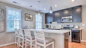 A modern kitchen with dark cabinets, a central island with bar stools, and built-in appliances. - Old Town Walkable Paradise w/ Private Patio! (Alexandria)