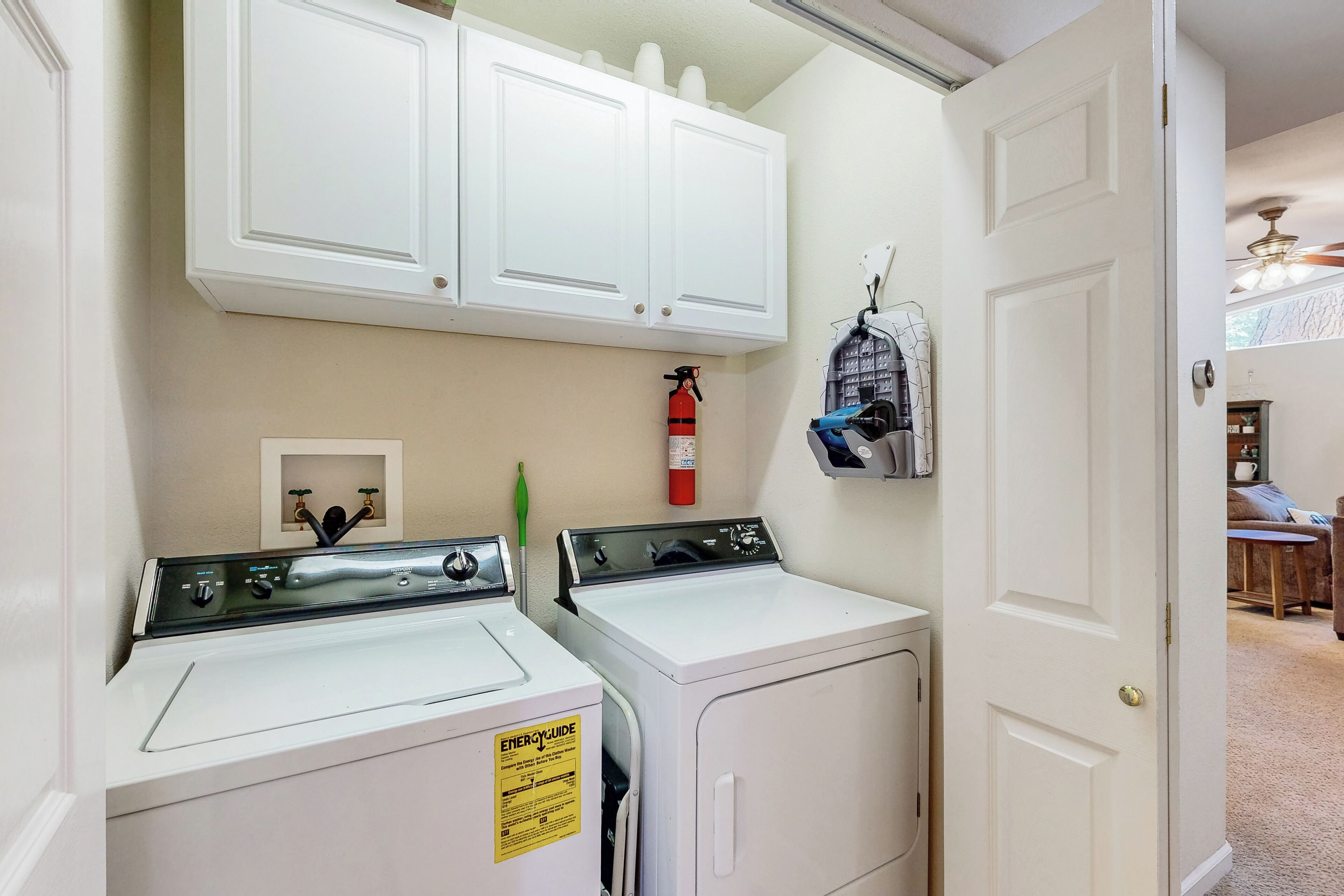 A laundry room with two washers and dryers, a fire extinguisher, and a small cabinet above the dryers.