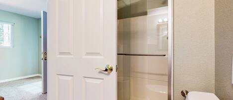 A bathroom with a glass shower enclosure, a white toilet, and a door with a gold handle.