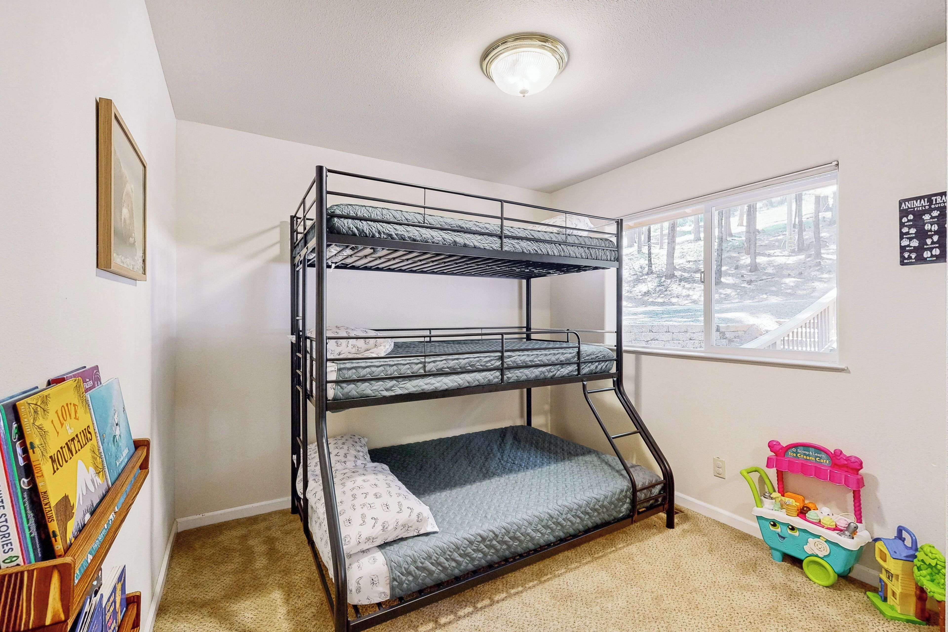 A bunk bed in a room with a window, a bookshelf, and a toy cart.