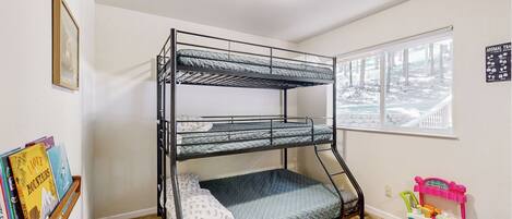 A bunk bed in a room with a window, a bookshelf, and a toy cart.