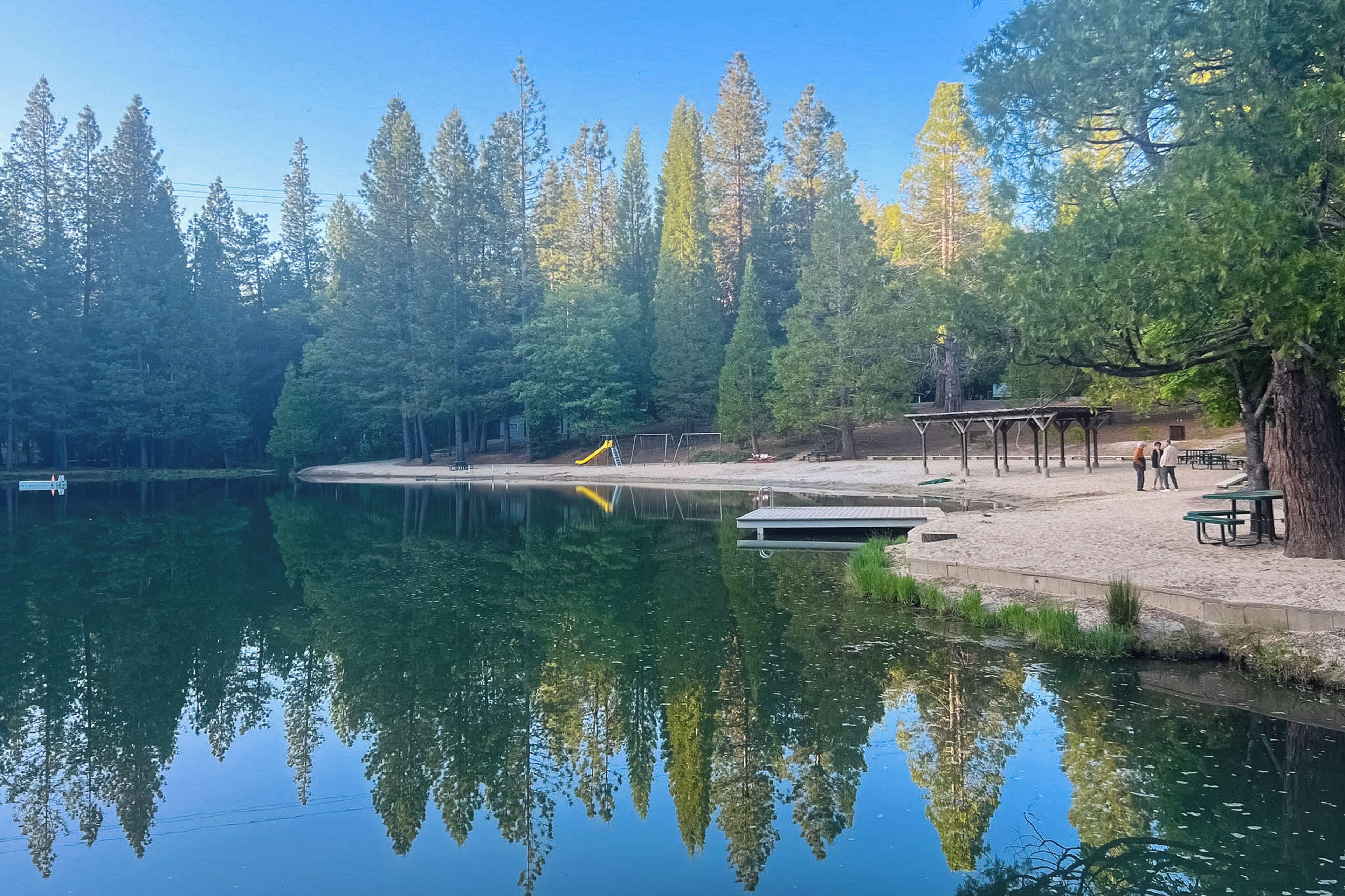 En lugn park vid sjön med ett trädäck, picknickbord och en lekplats.