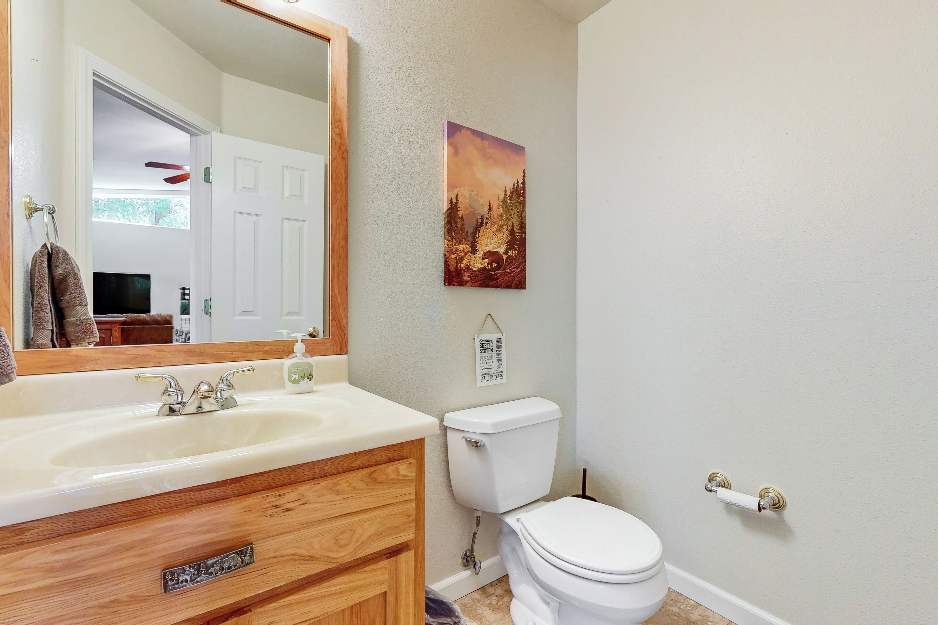 A bathroom with a wooden vanity, a sink, a toilet, and a framed picture on the wall.