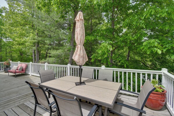 A deck with a table and chairs, surrounded by a white railing, set in a wooded area. - Waterfront W/hot Tub & Dock on Smith Mountain Lake (Goodview)