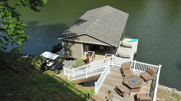 A lakeside deck with outdoor furniture, a covered area, and a dock extending into the water. - Private Hot Tub! Getaway on Smith Mountain Lake (Goodview)
