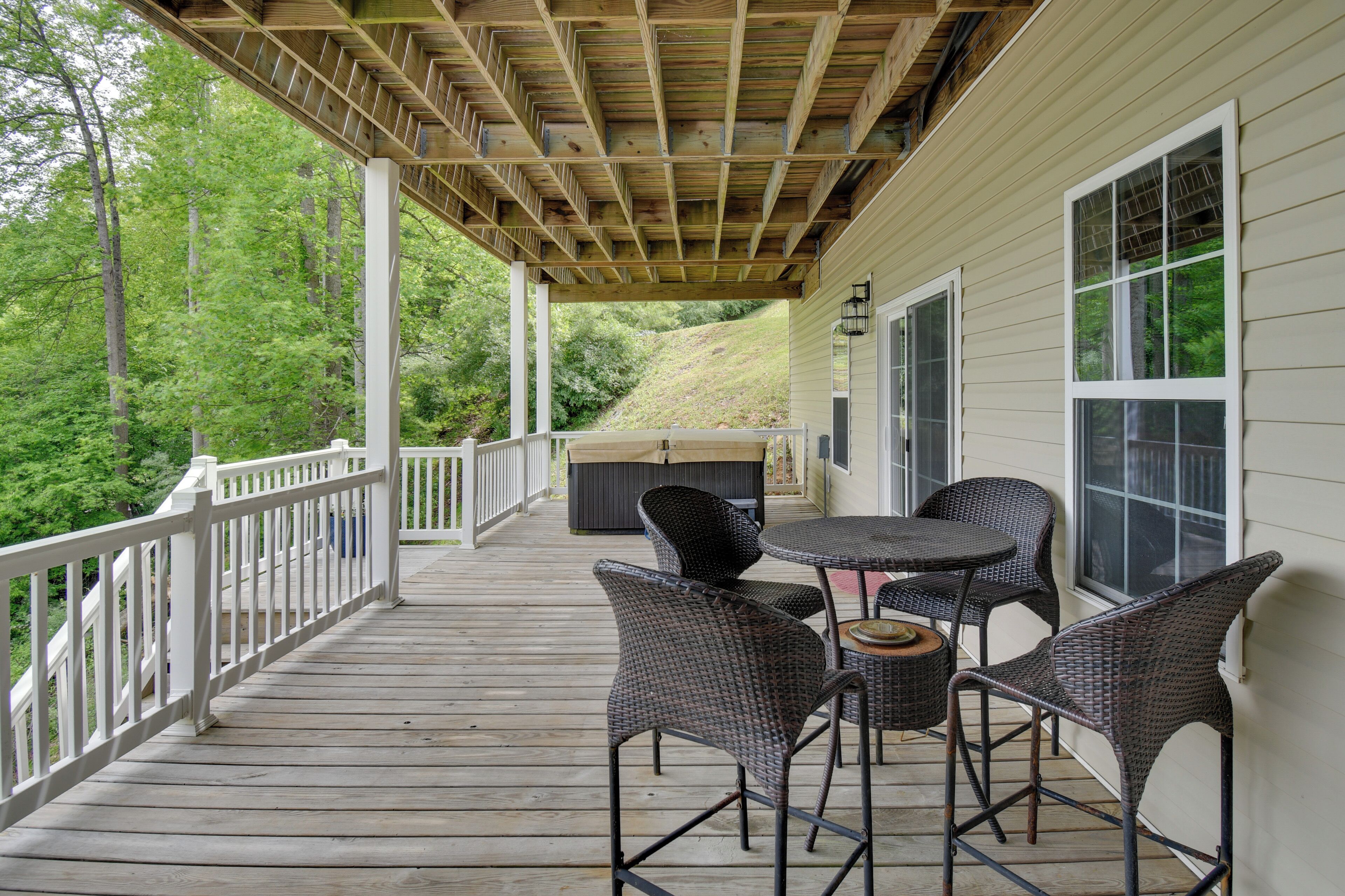 A covered outdoor deck with a wooden railing, wicker chairs, a small round table, and a barbecue grill.