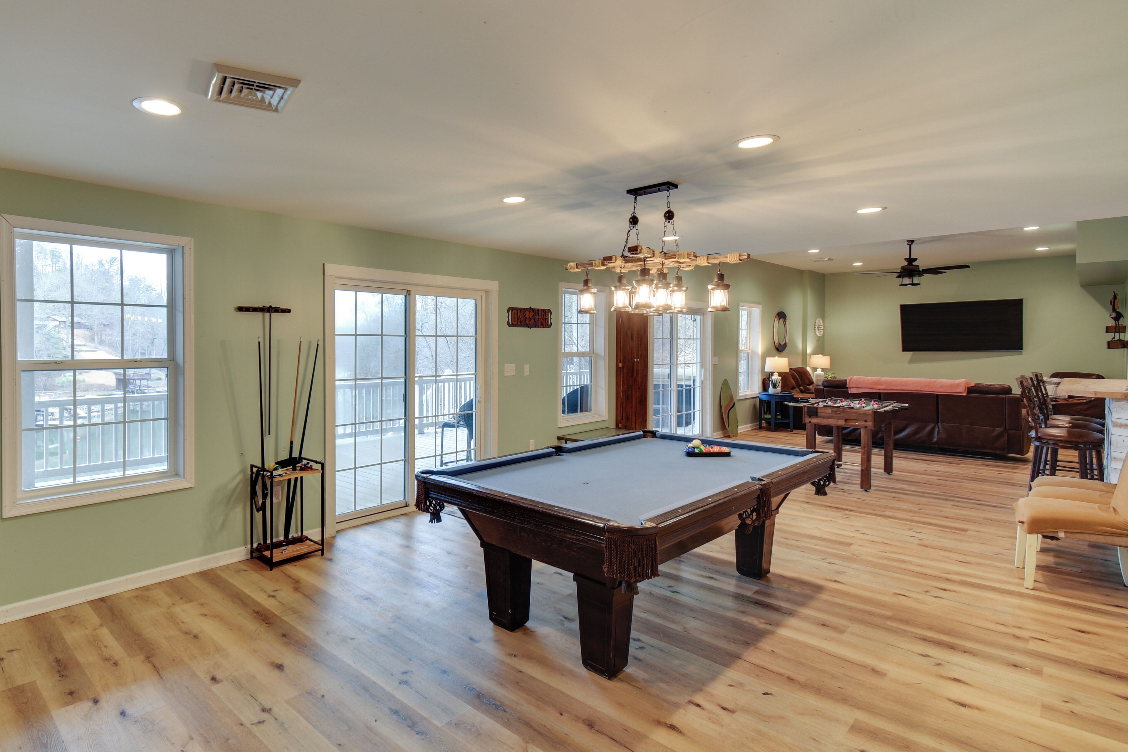 A spacious living room with a pool table, a dining area, and a large window offering a view.