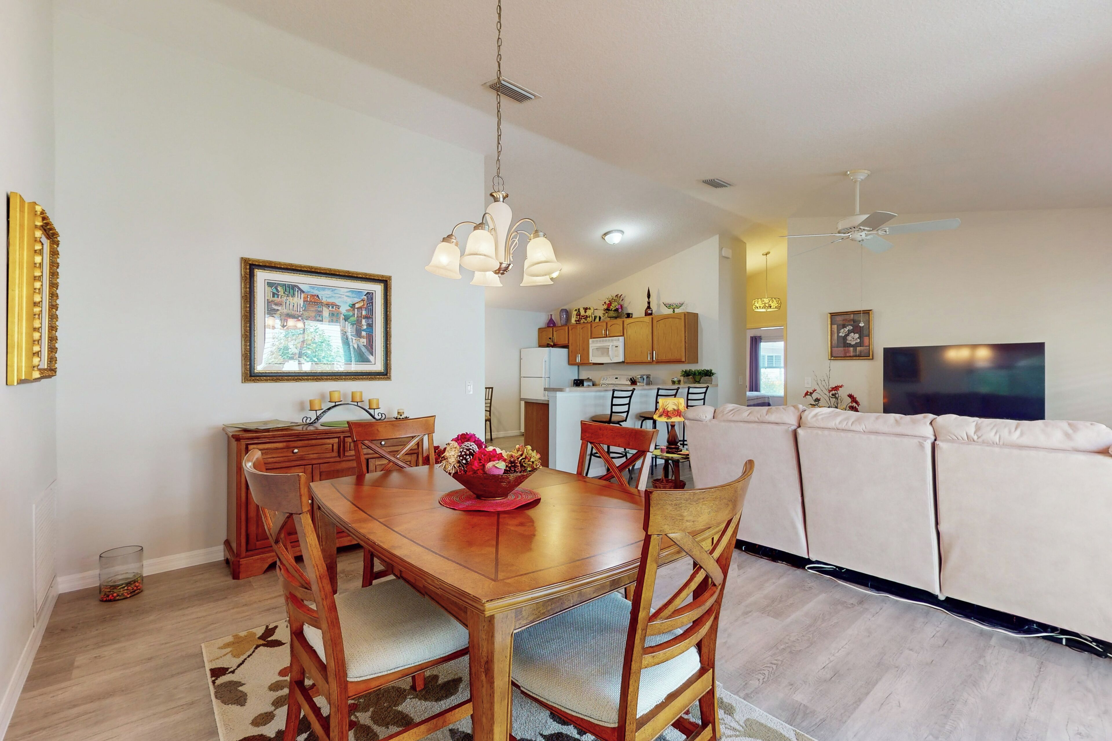 A dining area with a wooden table and chairs, a chandelier, and a painting on the wall.