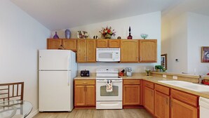 A kitchen with wooden cabinets, a white refrigerator, a microwave, an oven, and a sink. - Dog-friendly Home w/ Golf Cart, AC, Wifi (The Villages)