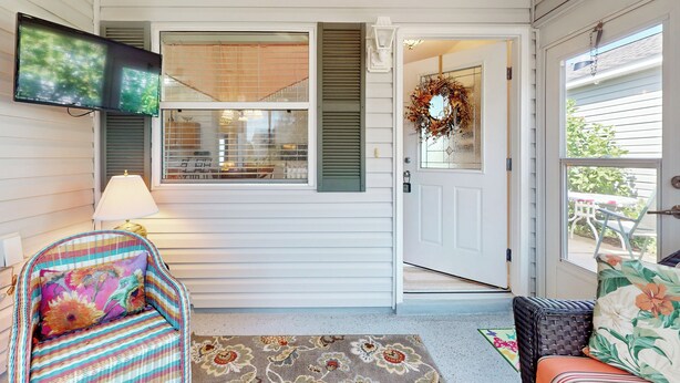 A porch with a television, a chair with a floral cushion, and a door with a wreath. - Dog-friendly Home w/ Golf Cart, AC, Wifi (The Villages)