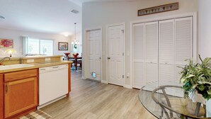 A modern kitchen with wooden cabinets, a dishwasher, and a dining area with a table and chairs. - Dog-friendly Home w/ Golf Cart, AC, Wifi (The Villages)