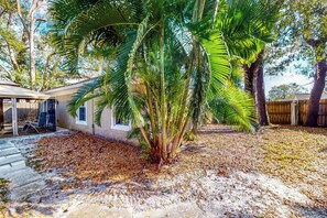 Une maison avec un patio couvert, un palmier et une clôture en bois en arrière-plan.