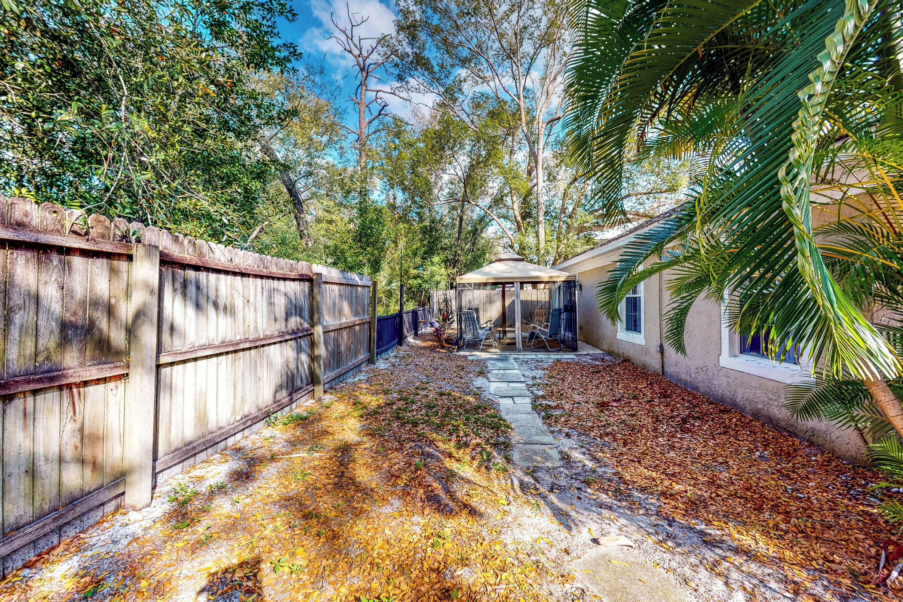 A backyard with a wooden fence, a patio area, and a house with windows.