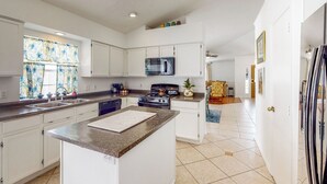 Una cocina moderna con armarios blancos, encimera de granito, refrigerador de acero inoxidable y microondas.