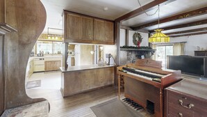 Amplia sala de estar con un piano de madera, televisión y una cocina al fondo.