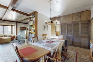 Un comedor con una mesa de madera, sillas y un mantel de encaje. Se observan estanterías y una biblioteca en el fondo.