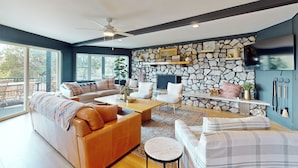 A modern living room with a stone wall, comfortable seating, a flat-screen TV, and a ceiling fan. - Buckthorn Beauty: Golf, Hike & More (Show Low)