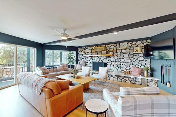 A modern living room with a stone wall, comfortable seating, a flat-screen TV, and a ceiling fan. - Buckthorn Beauty: Golf, Hike & More (Show Low)