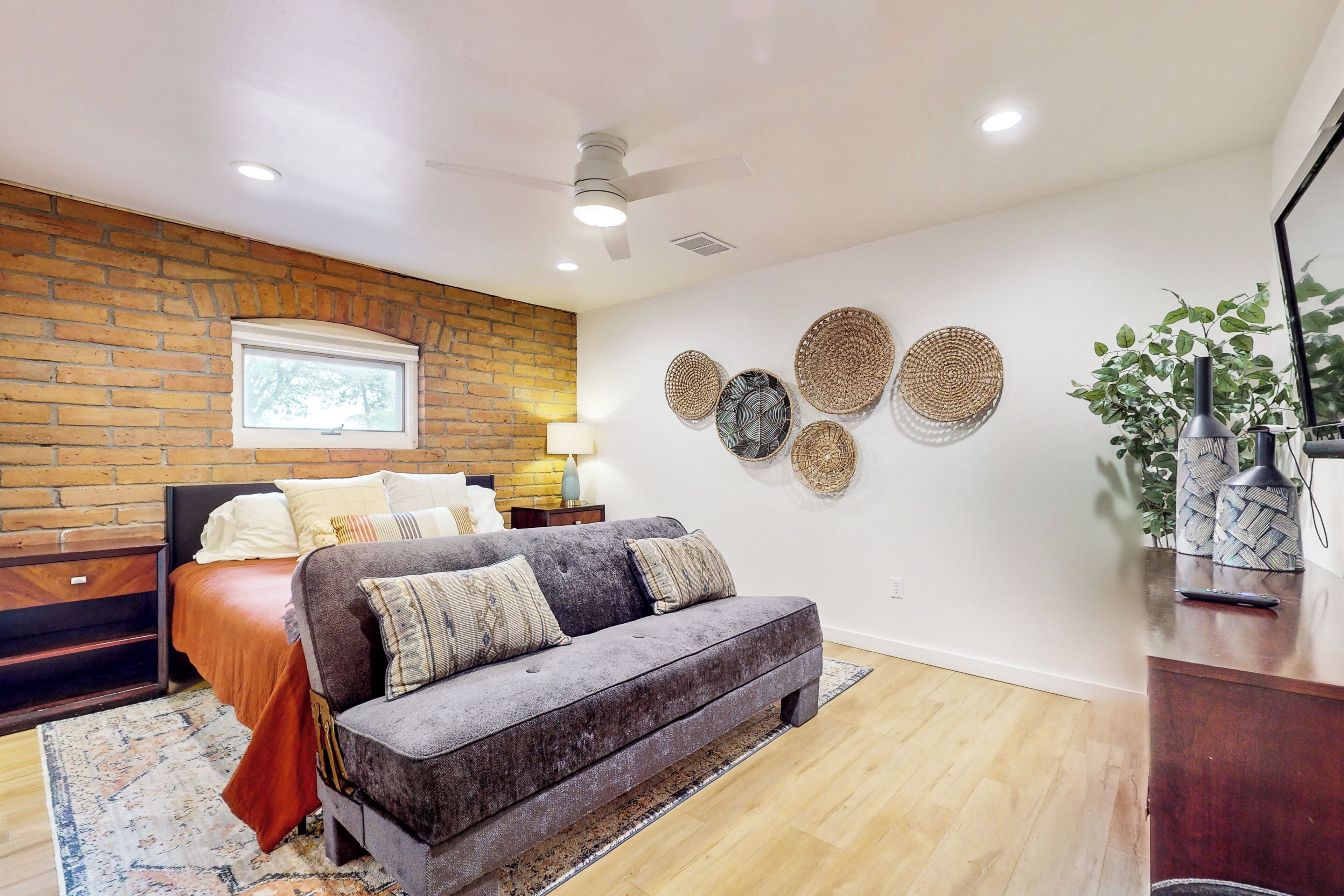 Un salon moderne avec un mur d’accent en briques, un canapé gris, un plancher en bois et des œuvres d’art décoratives accrochées au mur.