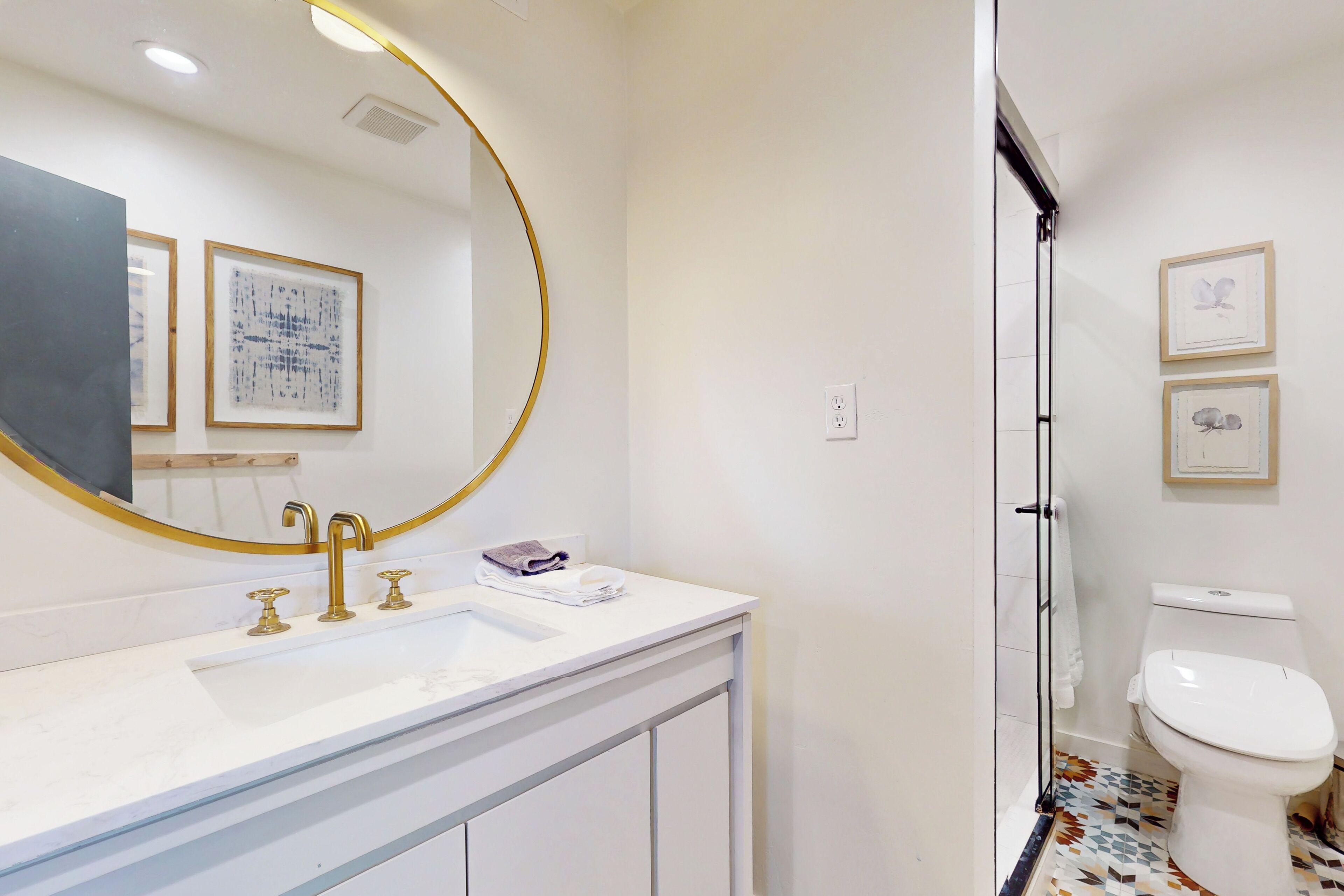 A bathroom with a white sink, gold faucets, a large mirror, and a toilet.