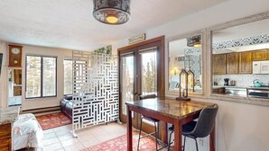 Un'ampia stanza con un tavolo da pranzo in legno, uno sgabello da bar e un divano. Uno schermo decorativo è all'ingresso, e si intravede un angolo cottura attraverso una porta aperta.
