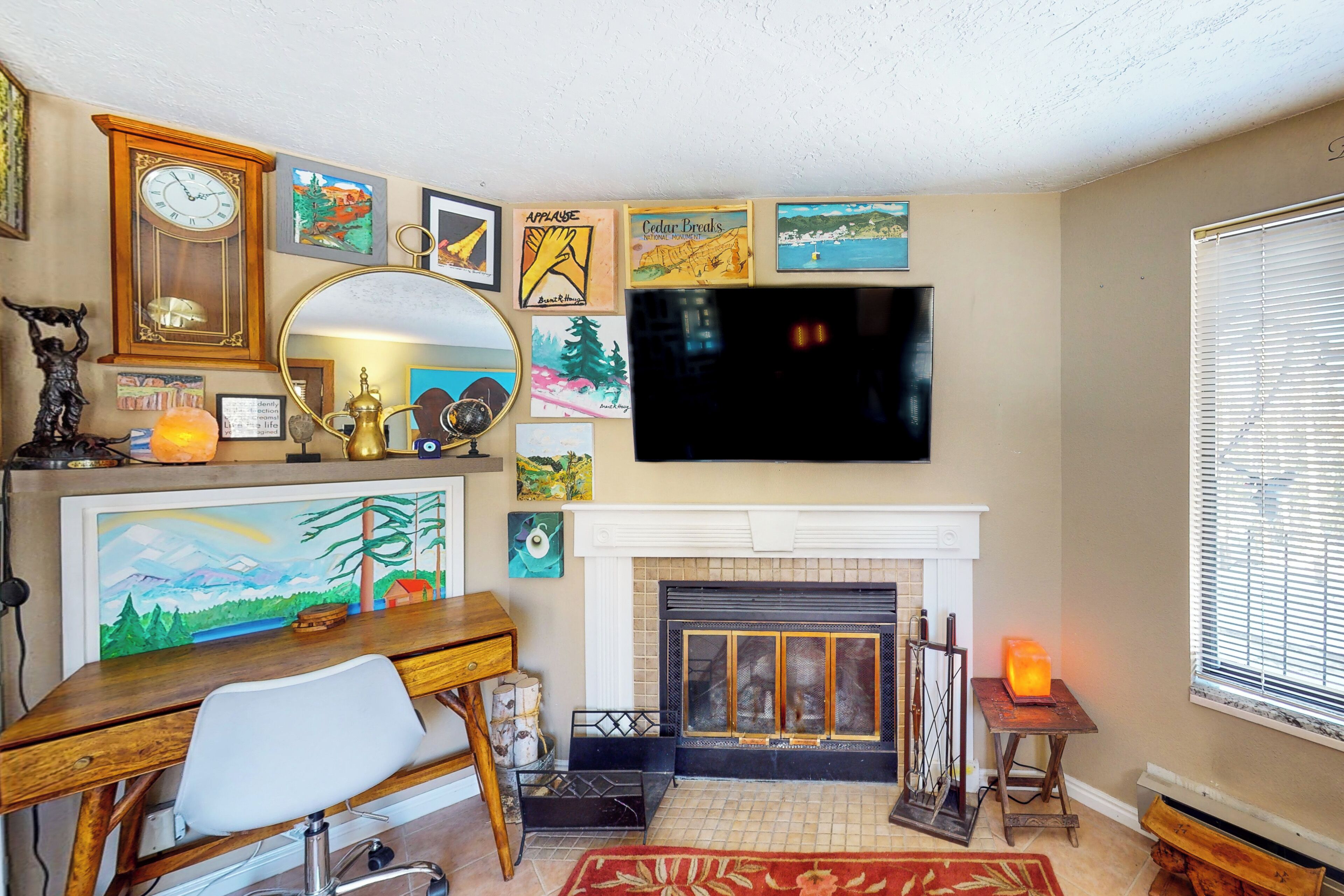A living room with a fireplace, a TV mounted above it, and various framed artworks on the walls.