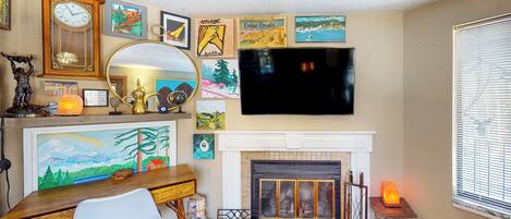 A living room with a fireplace, a TV mounted above it, and various framed artworks on the walls.