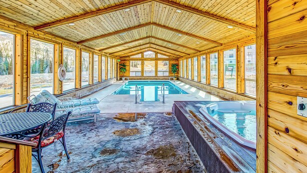 Una baita in legno con una grande piscina interna, una vasca idromassaggio e un'area pranzo con vista sull'esterno.