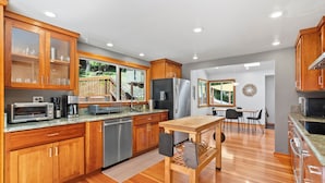 A modern kitchen with wooden cabinets, stainless steel appliances, and a wooden dining table. - Redwood Oasis - Luxe Santa Cruz Cabin w/ Hot Tub (Ben Lomond)