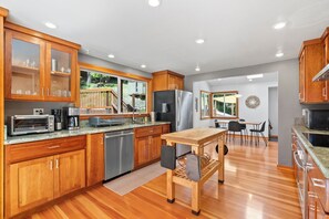 A modern kitchen with wooden cabinets, stainless steel appliances, and a wooden dining table. - Redwood Oasis - Luxe Santa Cruz Cabin w/ Hot Tub (Ben Lomond)