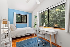 Un dormitorio con cama, escritorio, silla, ventana y una planta.