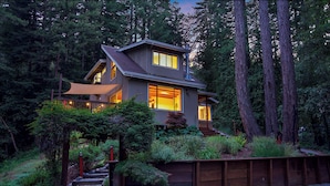A modern house with a sloped roof, large windows, and a wooden deck. - Redwood Oasis - Luxe Santa Cruz Cabin w/ Hot Tub (Ben Lomond)