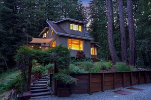 A modern house with a sloped roof, large windows, and a wooden deck. - Redwood Oasis - Luxe Santa Cruz Cabin w/ Hot Tub (Ben Lomond)