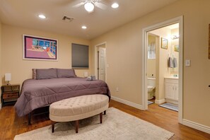 A bedroom with a large bed, a nightstand, a bedside table, a window with blinds, a ceiling fan, and a bathroom visible through an open door. - Near Parks, Shops & Eats! Bullhead City Casita (Bullhead City)