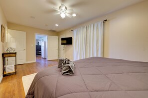 A bedroom with a large bed, a ceiling fan, a flat-screen TV, and a view of the kitchen through an open door. - Near Parks, Shops & Eats! Bullhead City Casita (Bullhead City)