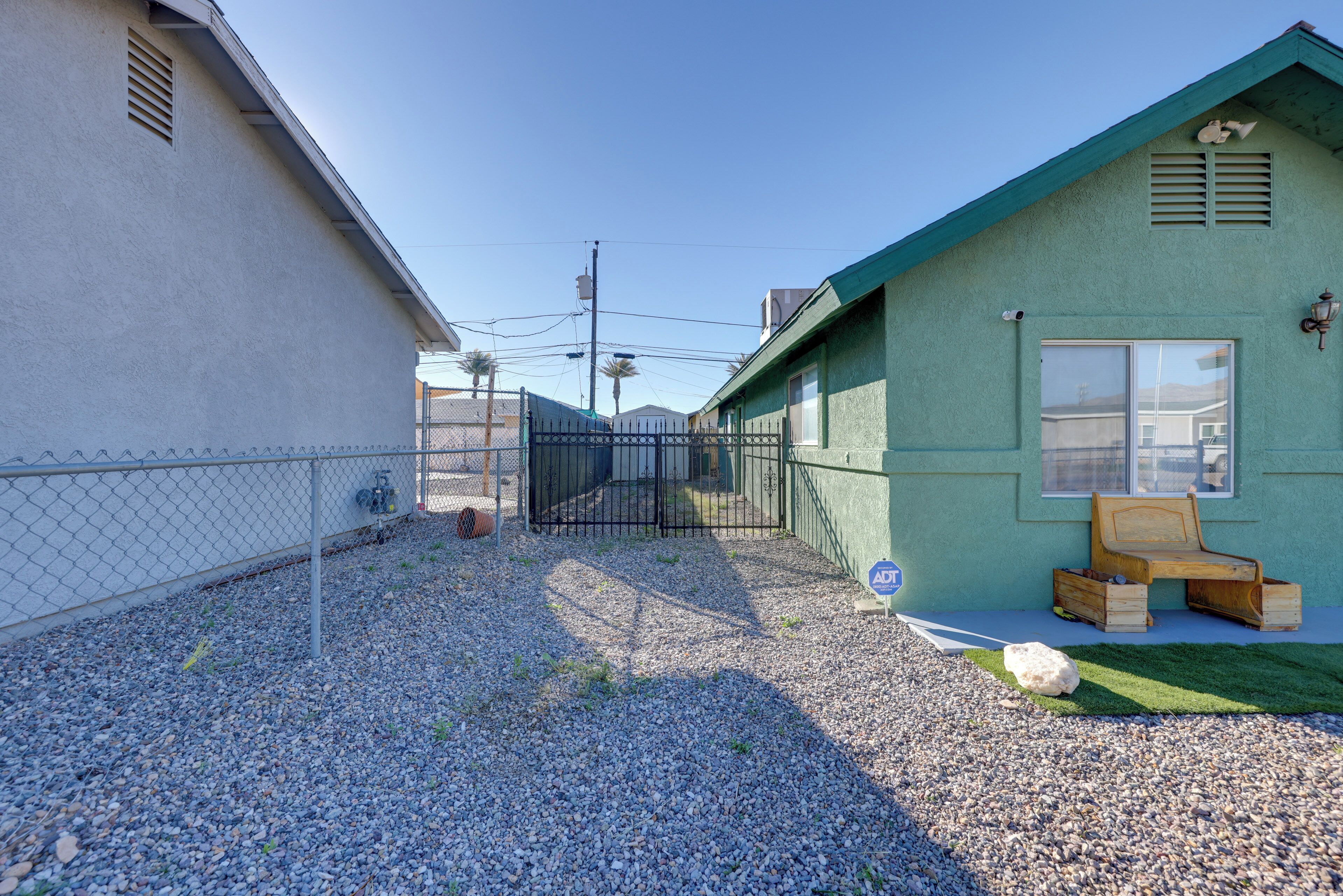 Zona residencial con patio cercado, un banco de madera pequeño y un edificio verde con una ventana y una puerta.