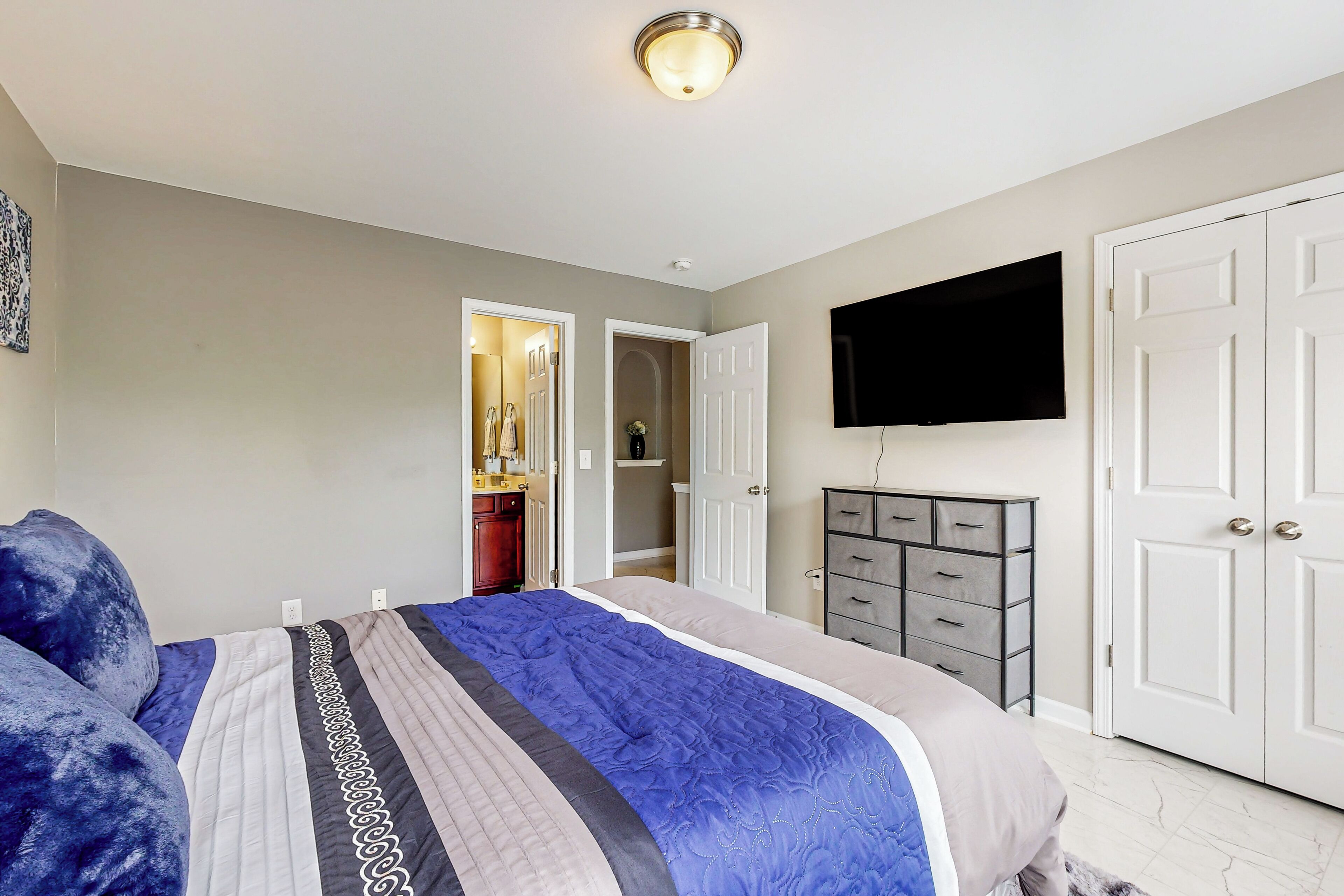 A bedroom with a large bed, a wardrobe, a television, and a door leading to a bathroom.