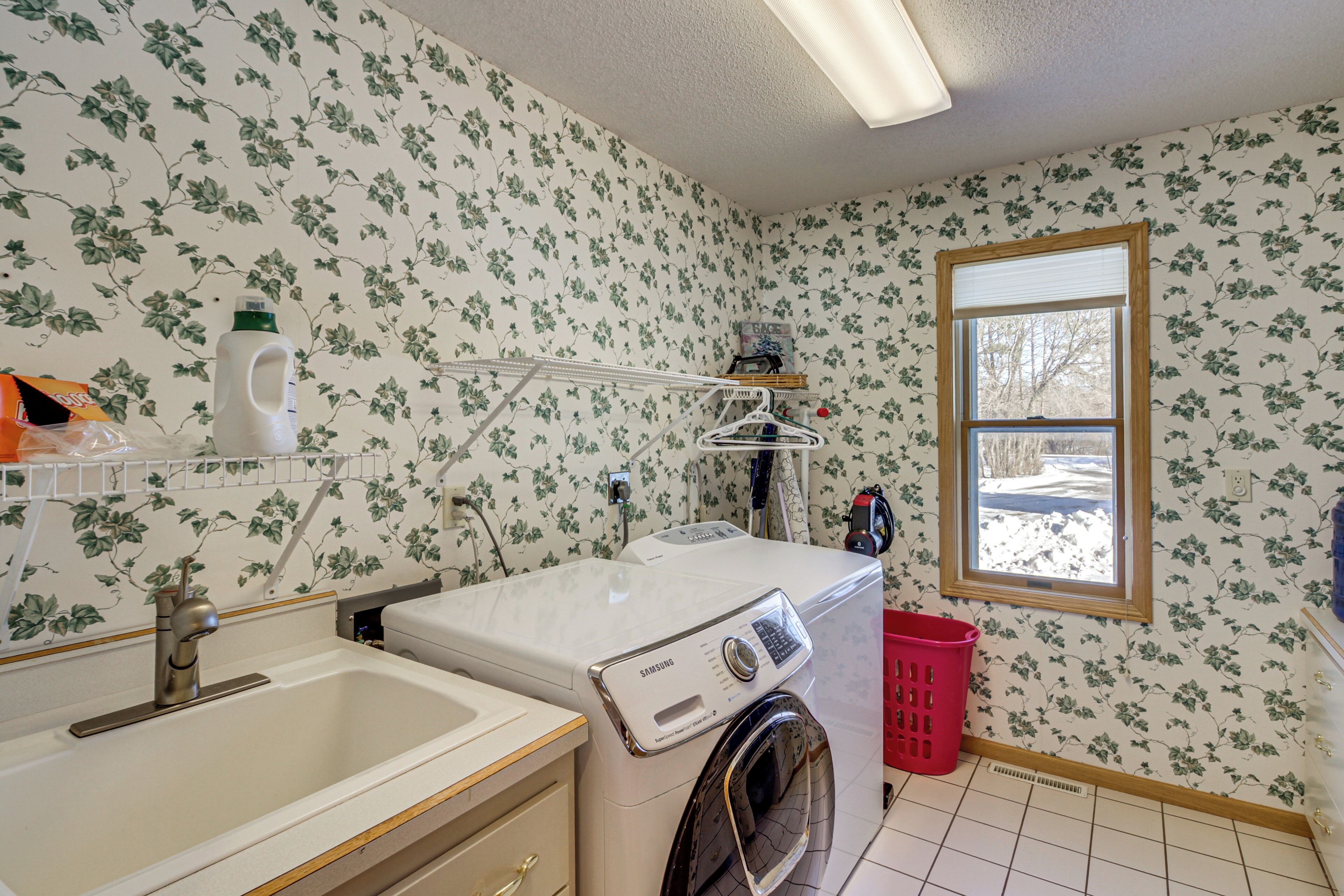A laundry room with a washing machine, a sink, and a window.