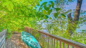 A wooden deck with a green kayak, surrounded by trees and overlooking a body of water. - Waterfront Alexandria Gem: Family & Group Friendly (Alexandria)