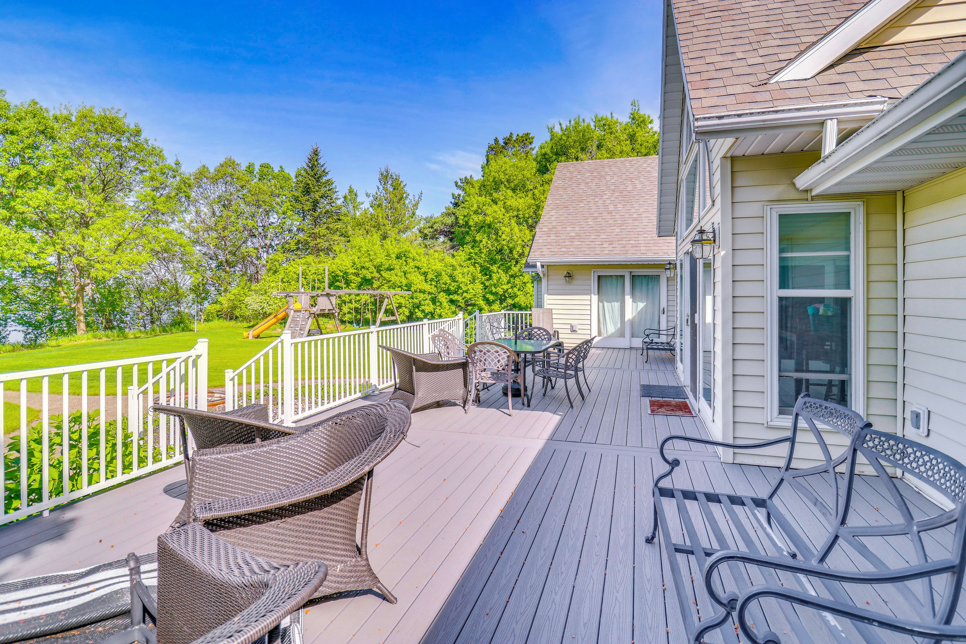 A deck with wicker furniture, a table, and chairs, overlooking a green landscape.