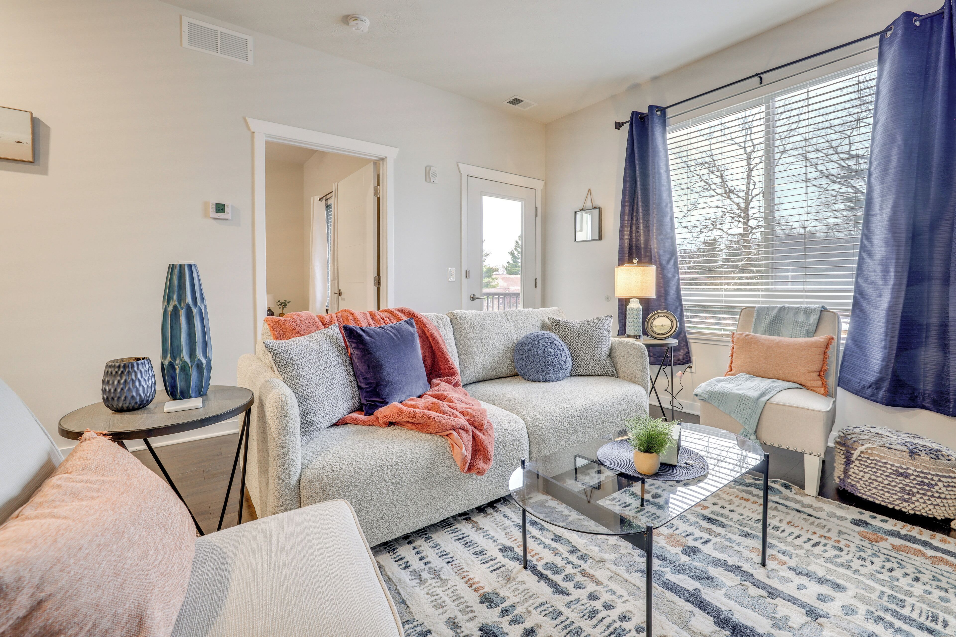 Ein gemütliches Wohnzimmer mit einer Couch, einem Sessel, einem Couchtisch und Blick ins Freie durch ein Fenster.