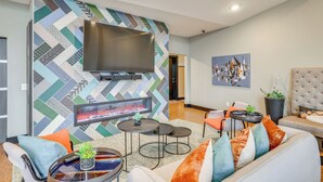 Un salon moderne doté d’un grand téléviseur à écran plat fixé sur un mur orné d’un motif géométrique, d’une cheminée et d’un coin salon confortable avec un canapé et des fauteuils.