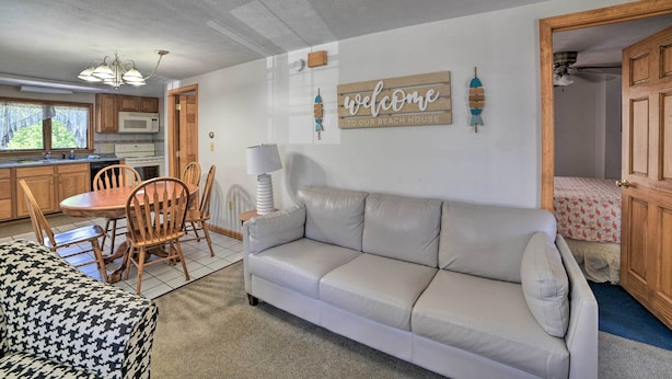 A cozy living area with a sofa, a dining table with chairs, a kitchen with wooden cabinets, and a 'welcome to our beach house' sign. - Apt. Walking Distance to OOB Pier & Saco Bay! (Old Orchard Beach)