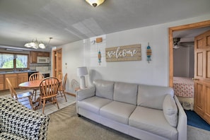 Un salon chaleureux avec un canapé, une table à manger et des chaises, une cuisine avec des meubles en bois et une pancarte indiquant : « Bienvenue dans notre maison de vacances en bord de mer ».
